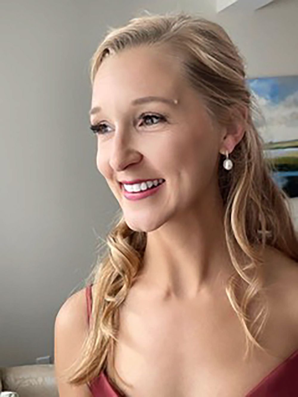 Smiling blonde woman in a maroon dress, looking to the side indoors