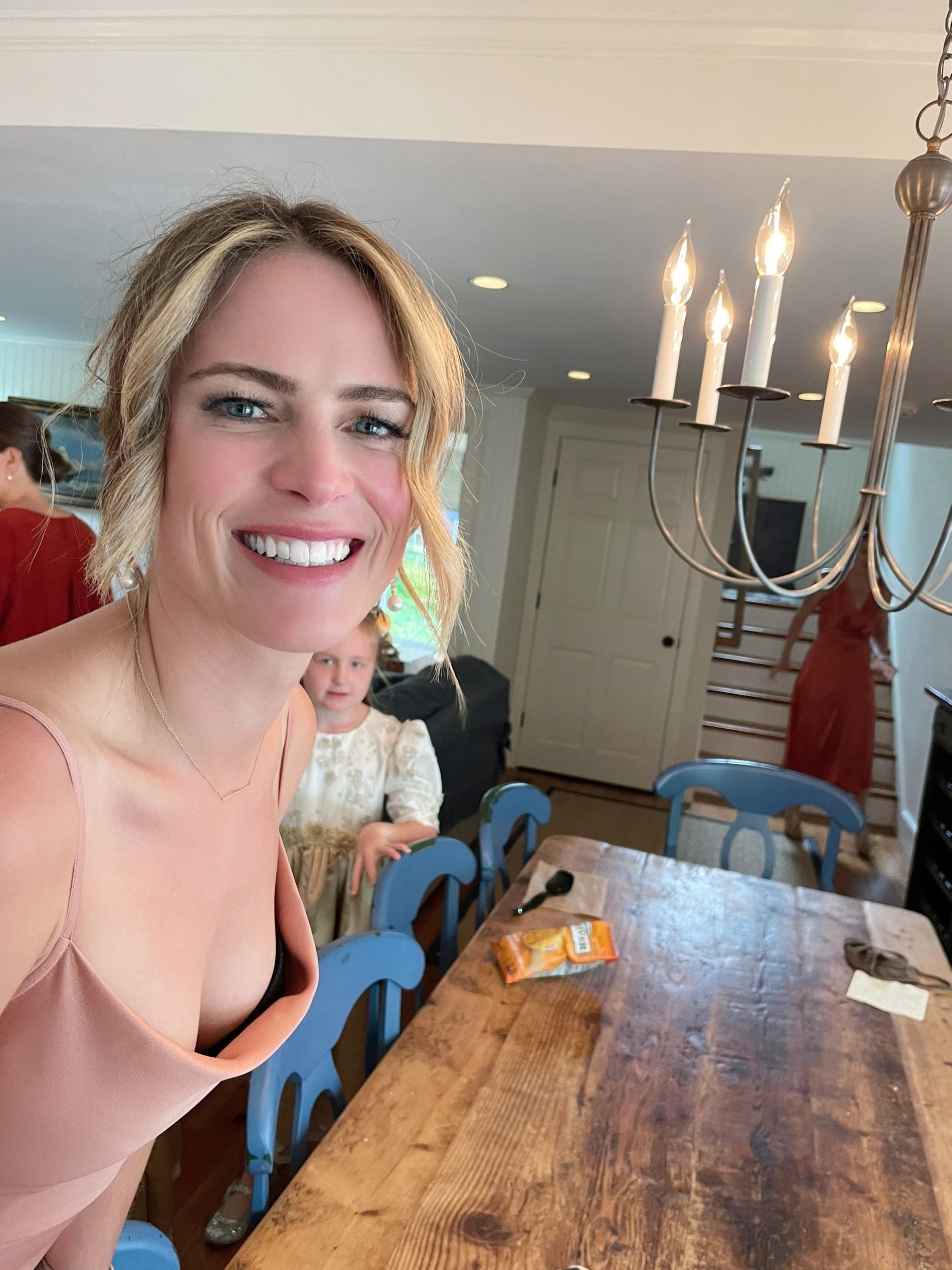 Smiling woman seated at a wooden table in a bright dining room with hanging pendant lights
