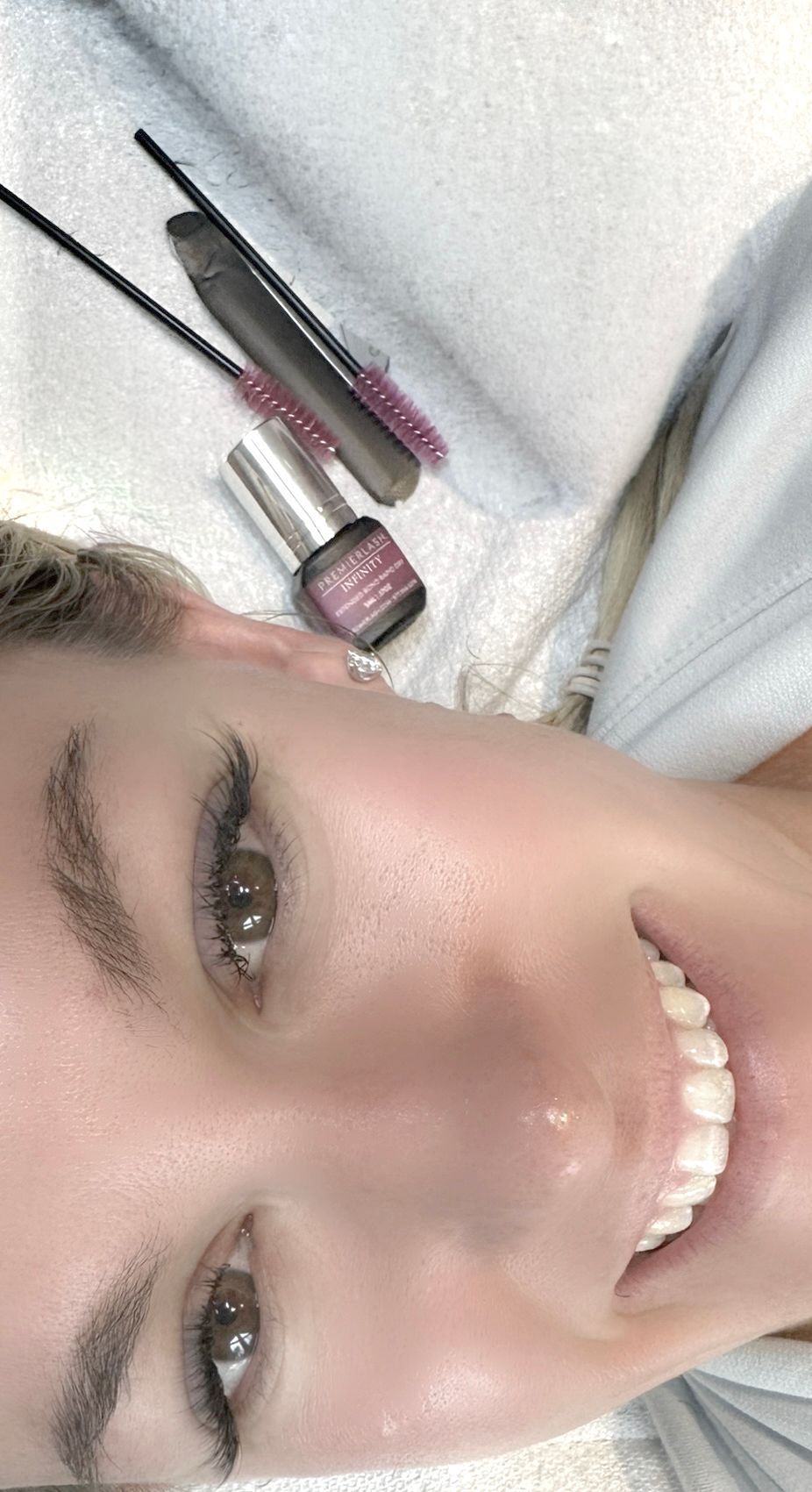 Smiling face with makeup products beside the cheek on a white towel background