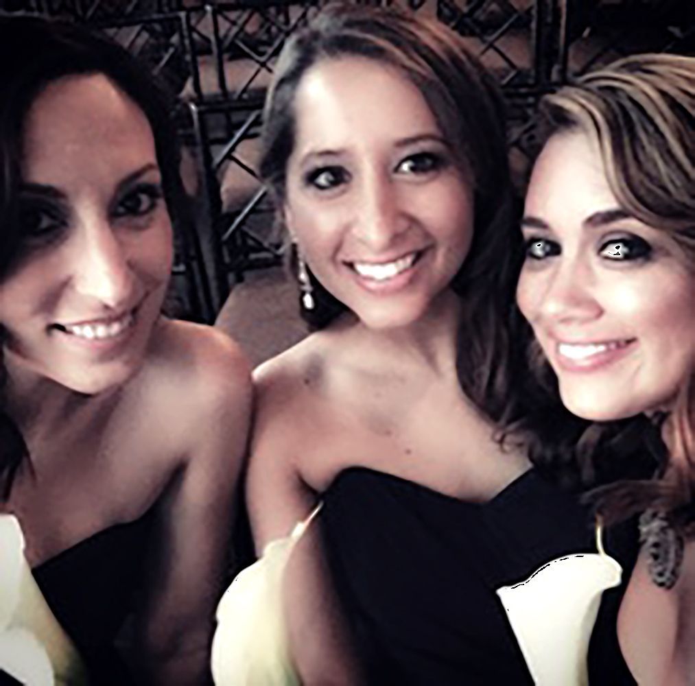Three smiling people posing closely together in a dim indoor setting.