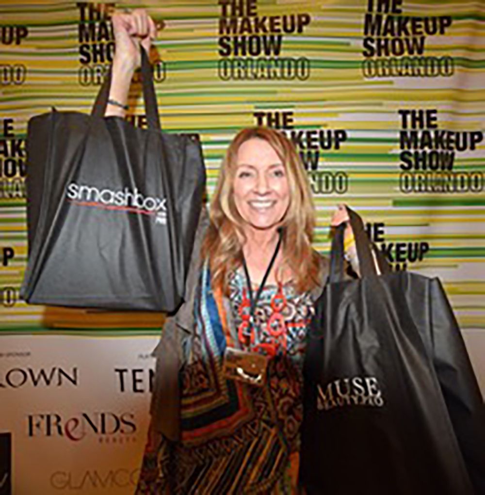Woman holding up shopping bags at The Makeup Show event backdrop