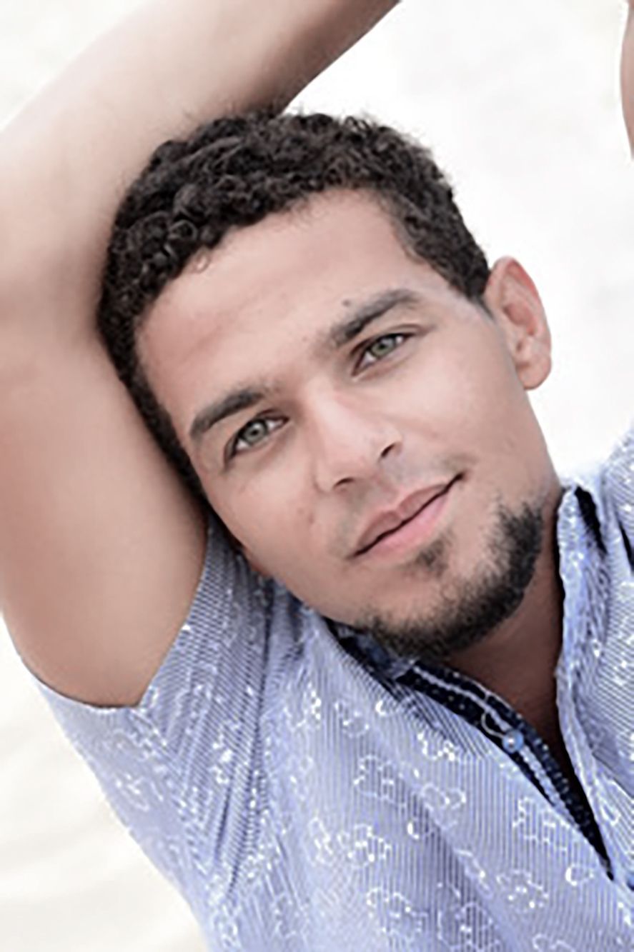 Portrait of a person leaning with one arm raised, wearing a light blue patterned shirt and a slight smile