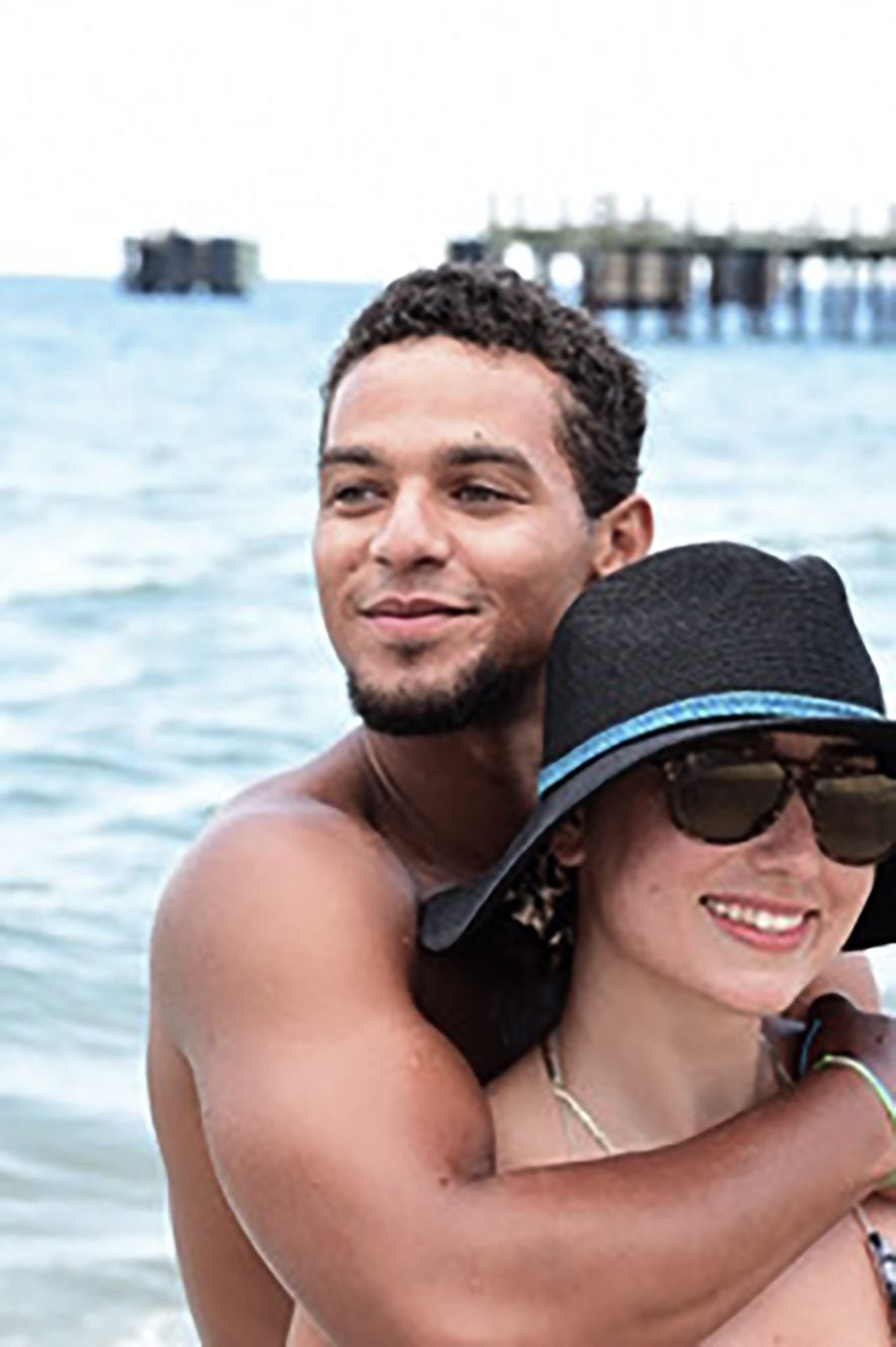 Two people smiling and hugging in the water, with a pier in the background.