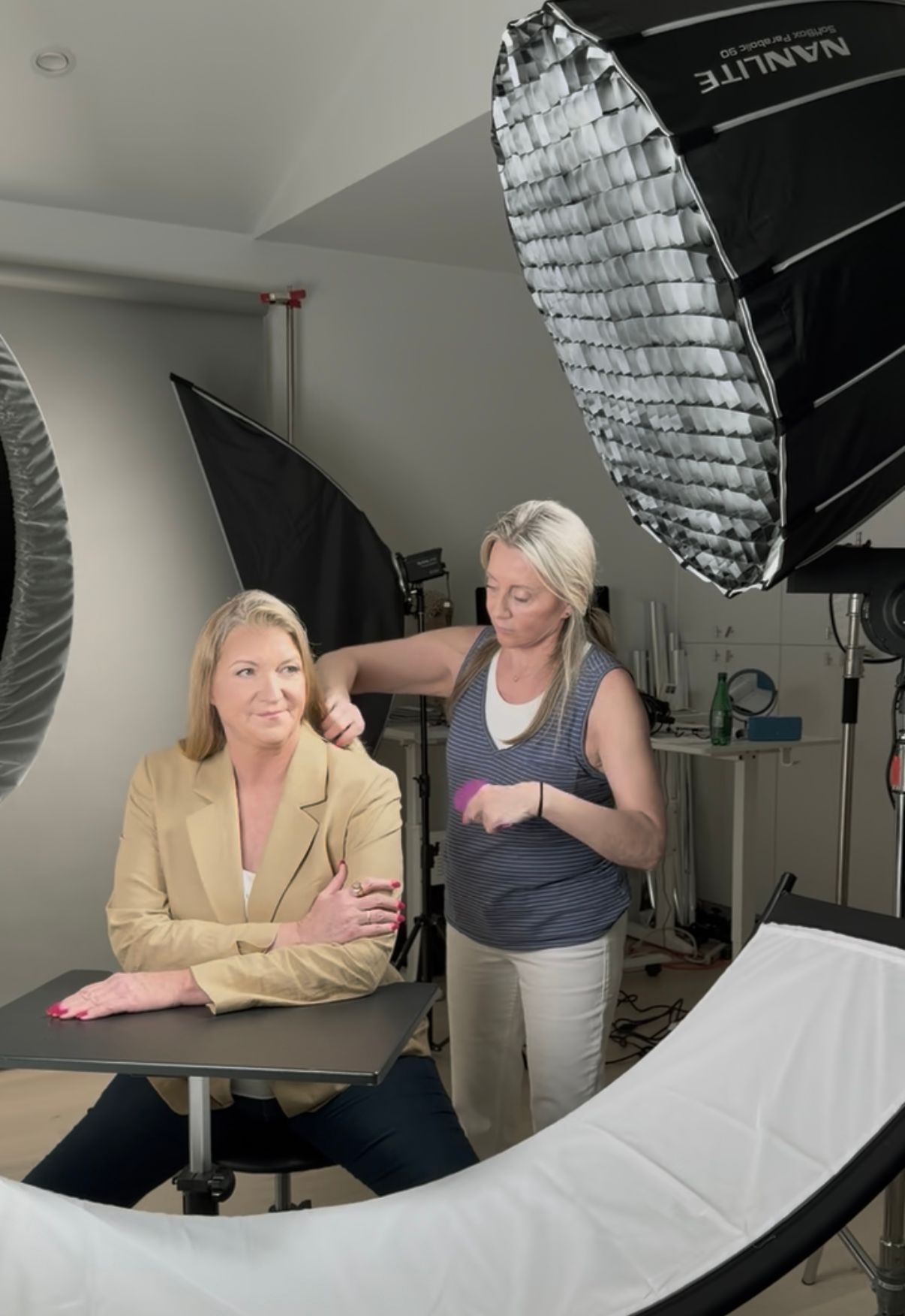 Two women in a photography studio posing before softbox lights and a curved white backdrop.