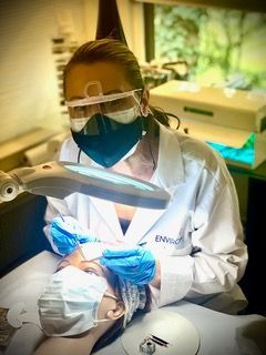 Dentist in white coat and mask examining a patient under a bright exam lamp