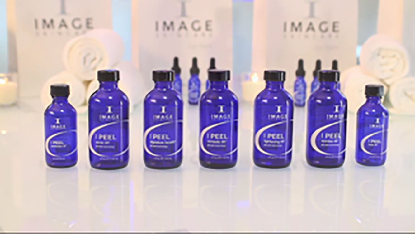 Blue glass skincare bottles arranged on a reflective surface with soft floral decor in the background