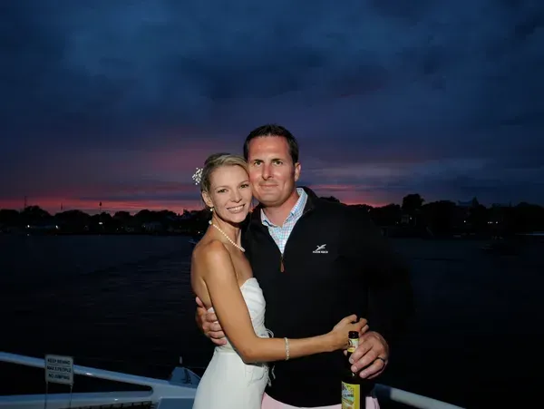 A couple embraces on a boat deck at twilight, with a dark sky and sunset glow over the water in the background.
