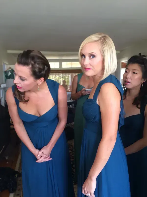 Three women in matching blue gowns stand in a room, with one facing the camera and two looking toward the left.