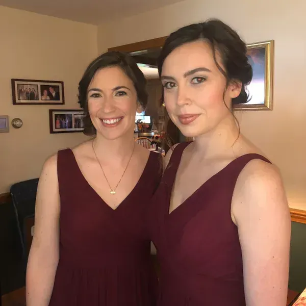 Two individuals wearing matching dark red dresses and styled hair, posing together indoors.