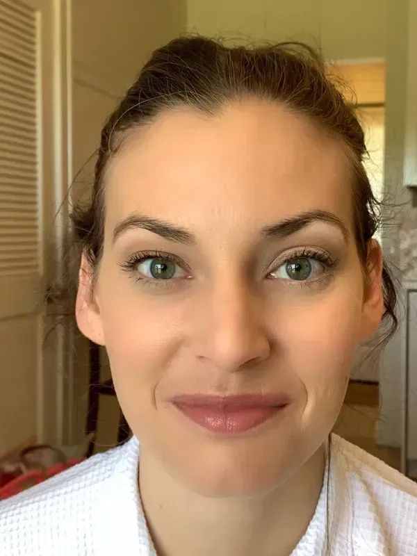 A person with light skin and dark hair worn up, looking directly at the camera with a calm, neutral expression.