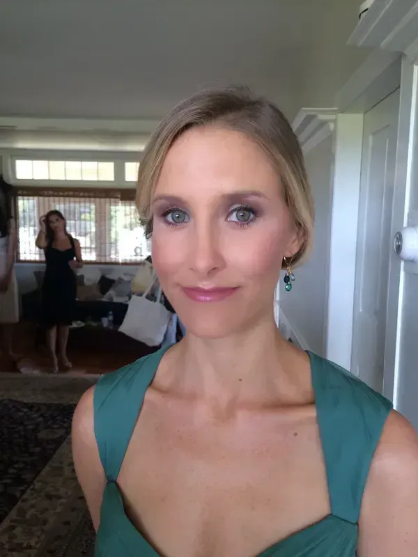 A person wearing a teal dress and earrings poses for a portrait in an indoor setting with a blurred background.