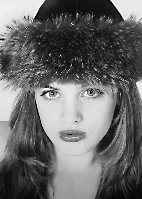 A close-up portrait of a person with long hair wearing a wide, dark, textured fur hat, looking directly at the camera.