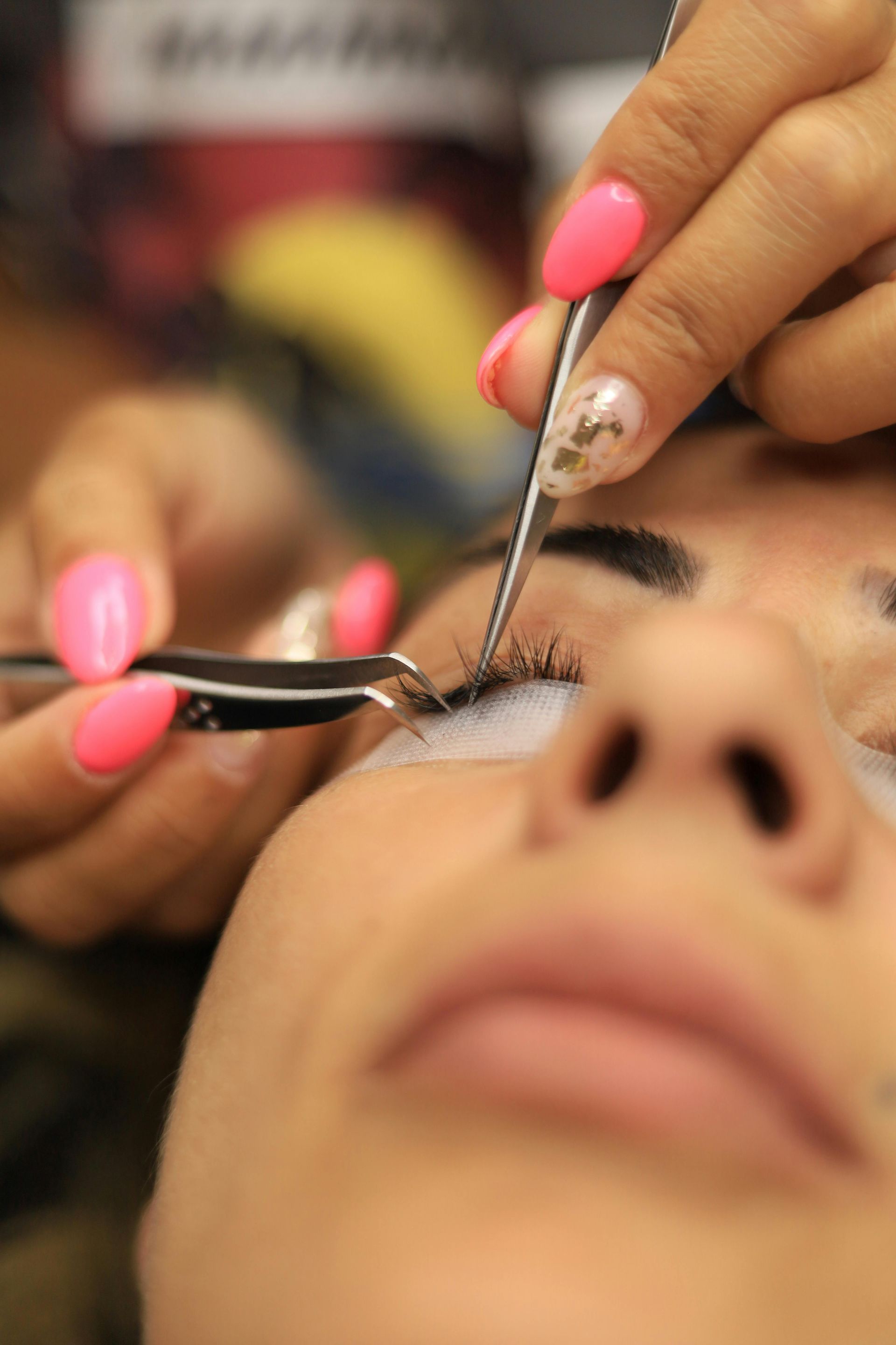 A close-up of a technician using tweezers to carefully apply individual eyelash extensions to a client's eye.