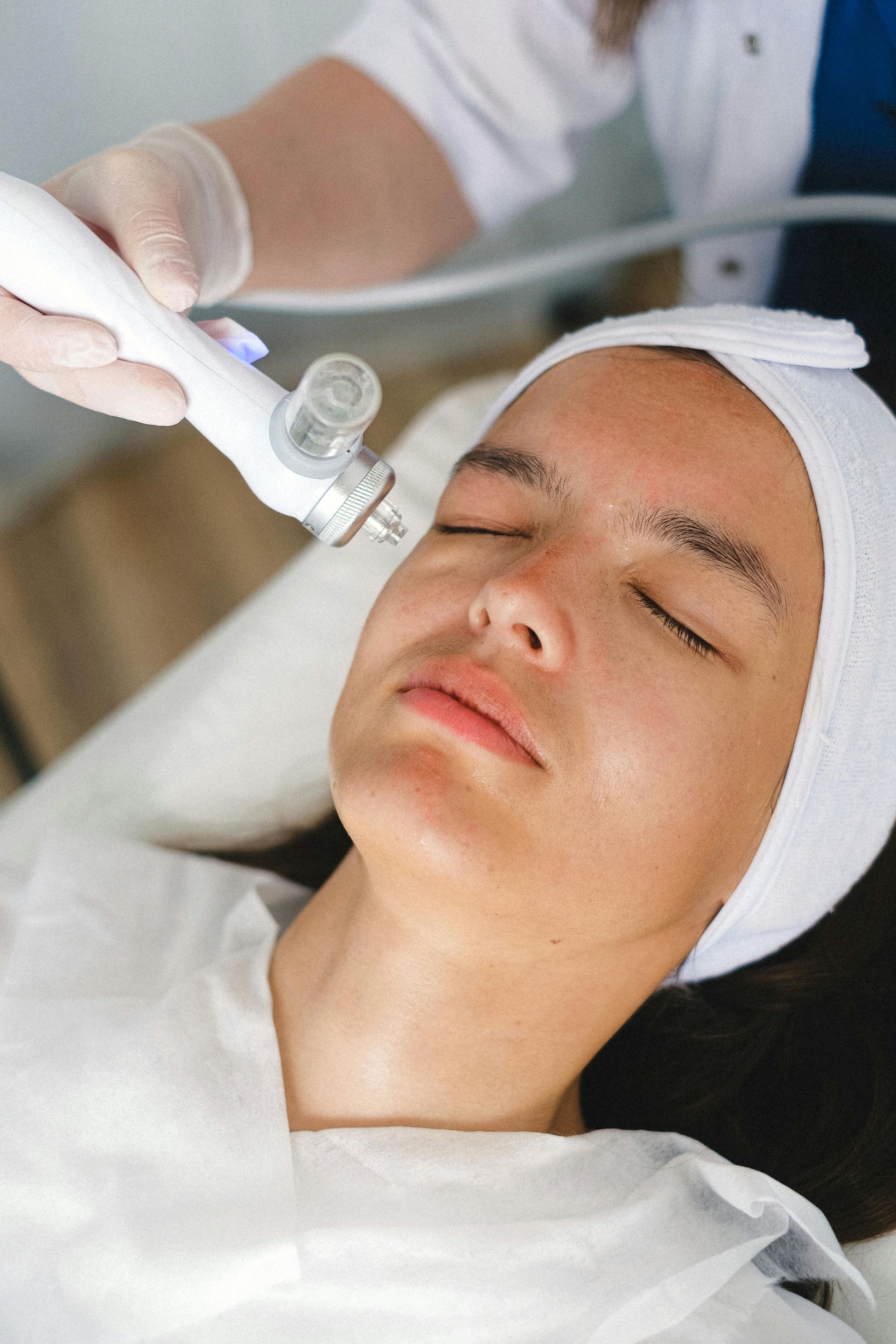 A person in a headband receives a facial treatment with a handheld vacuum device in a clinical setting.