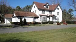 White two-story house with a red roof, driveway, and green lawn under a clear blue sky