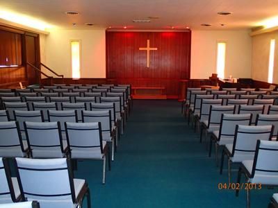 Empty chapel with rows of chairs facing a red altar wall and cross.