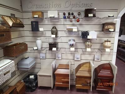 Display of decorative urns and memorial accessories on white wall shelves in a showroom.