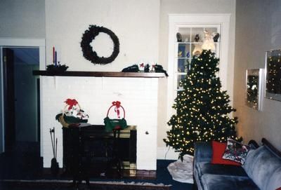 Living room with a decorated Christmas tree, fireplace mantle, and holiday wreath on the wall