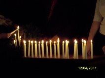 Row of lit candles in a dark room, with two people partially visible at the edges.