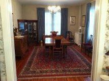 Dining room with a large red rug, wooden table and chairs, cabinet, and window with curtains.