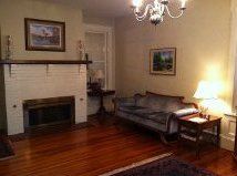 Cozy living room with fireplace, hardwood floors, gray sofa, side table lamp, and framed wall art