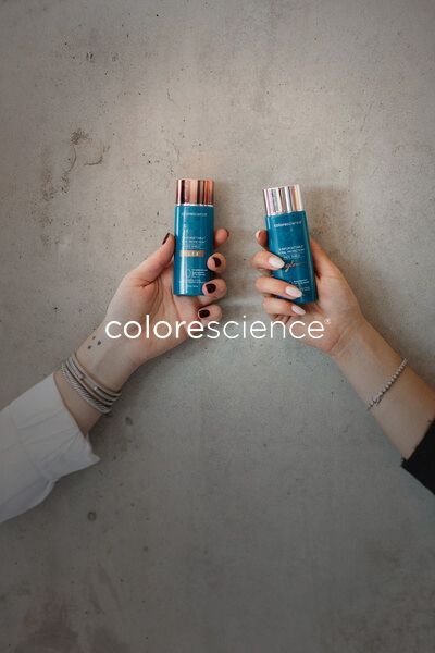 Two hands holding blue lip balm tubes against a gray wall.
