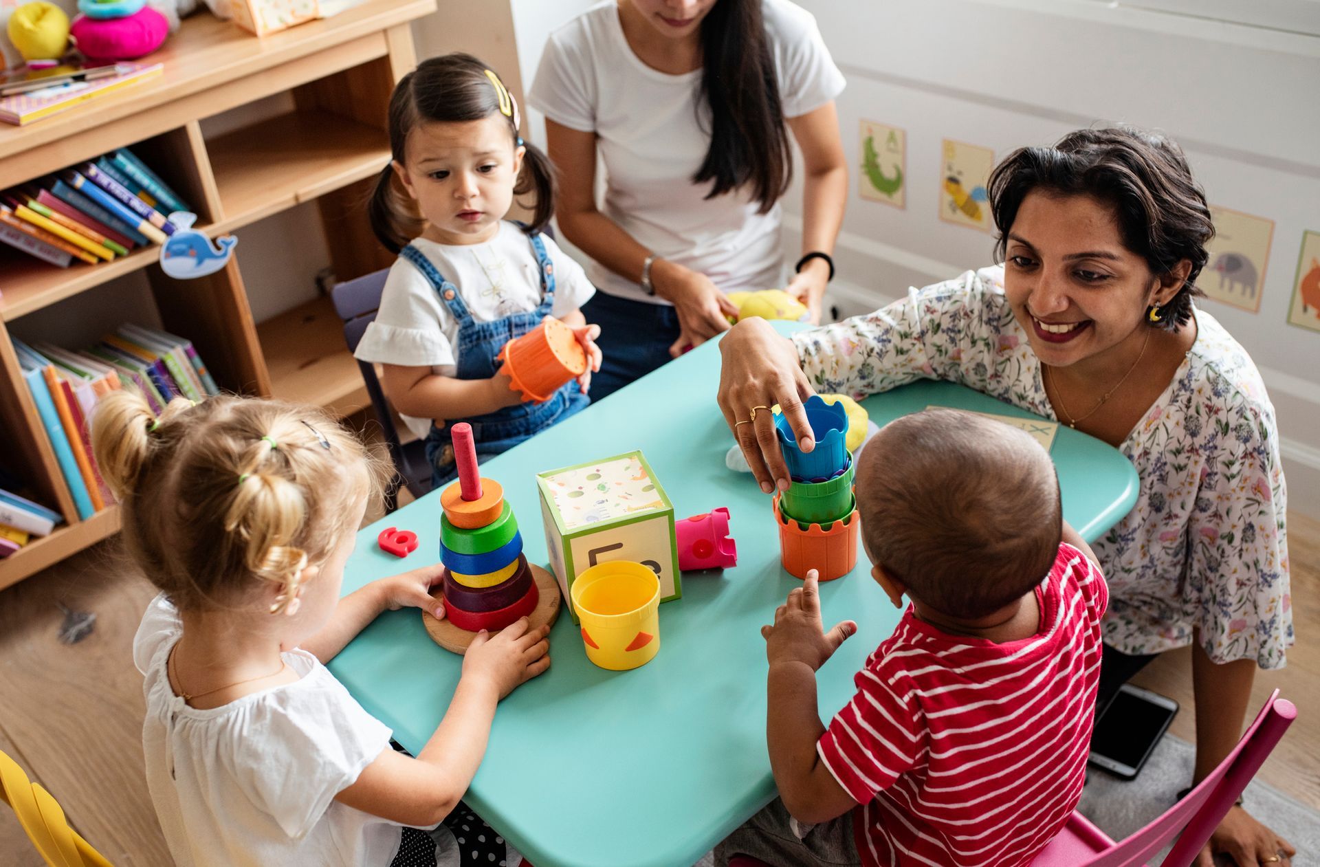 Toddlers are playing with the teacher in a colorful classroom.