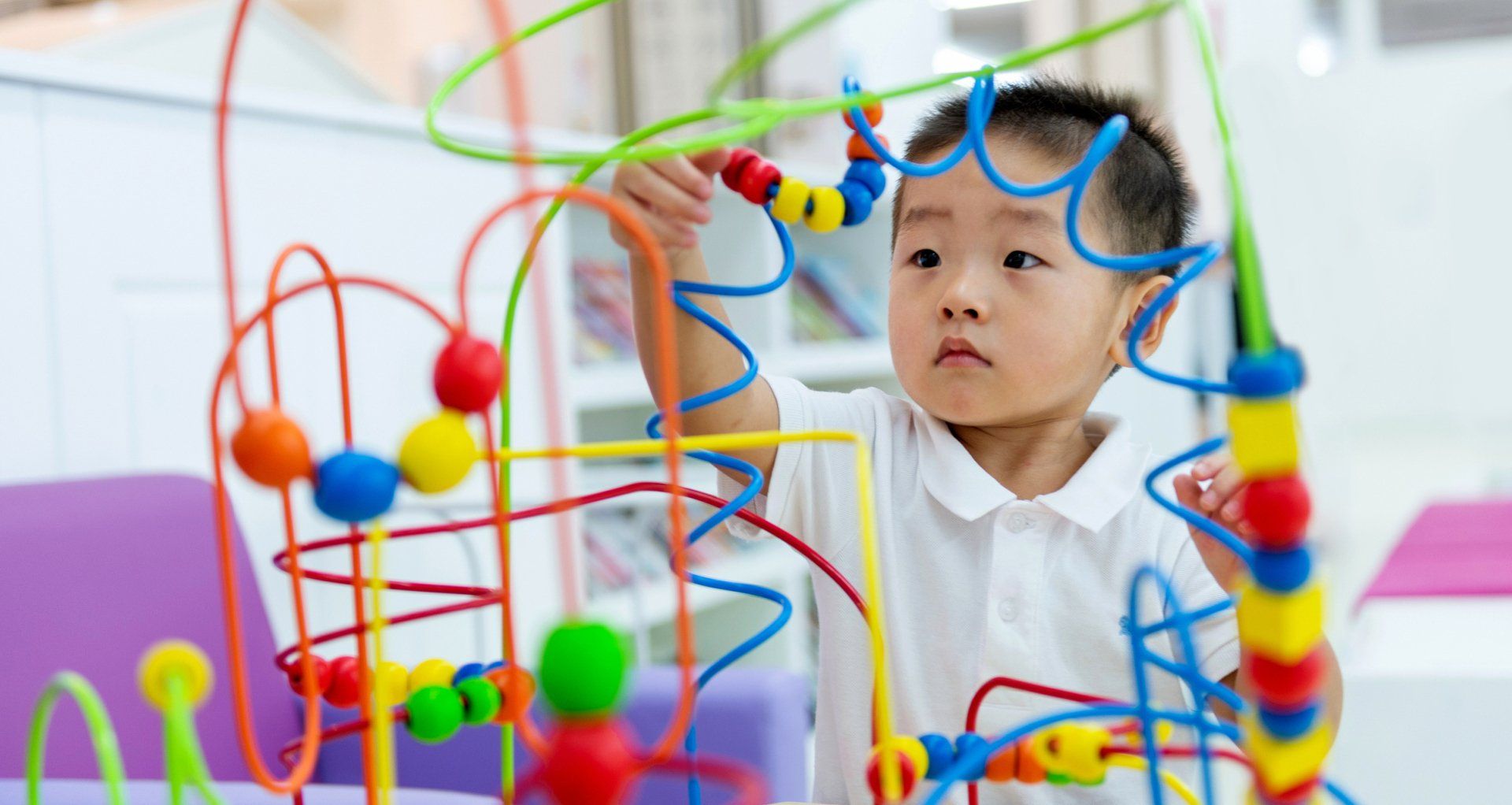 Young child focused on a colorful bead maze.