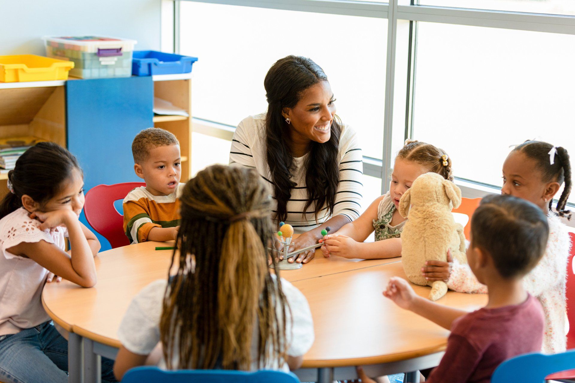 Teacher sits at round table with young children.