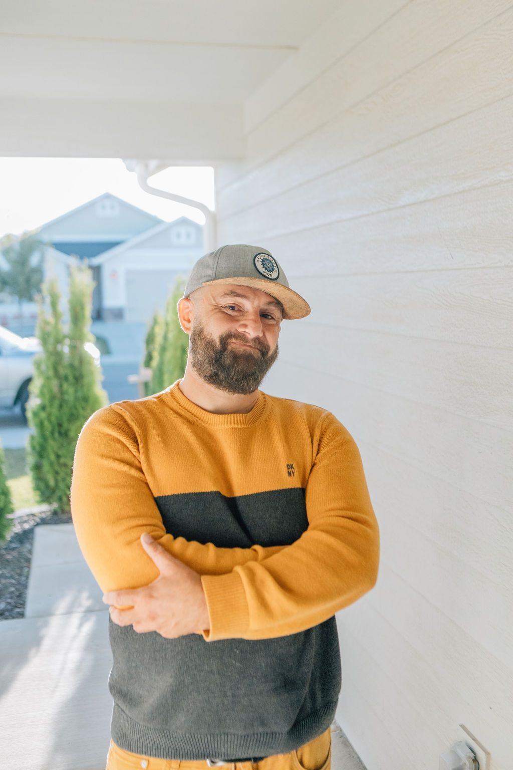 A man with a beard is wearing a yellow and black sweater and a hat.