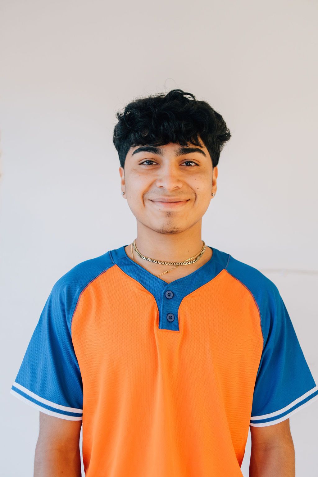A young man wearing an orange and blue shirt is smiling for the camera.
