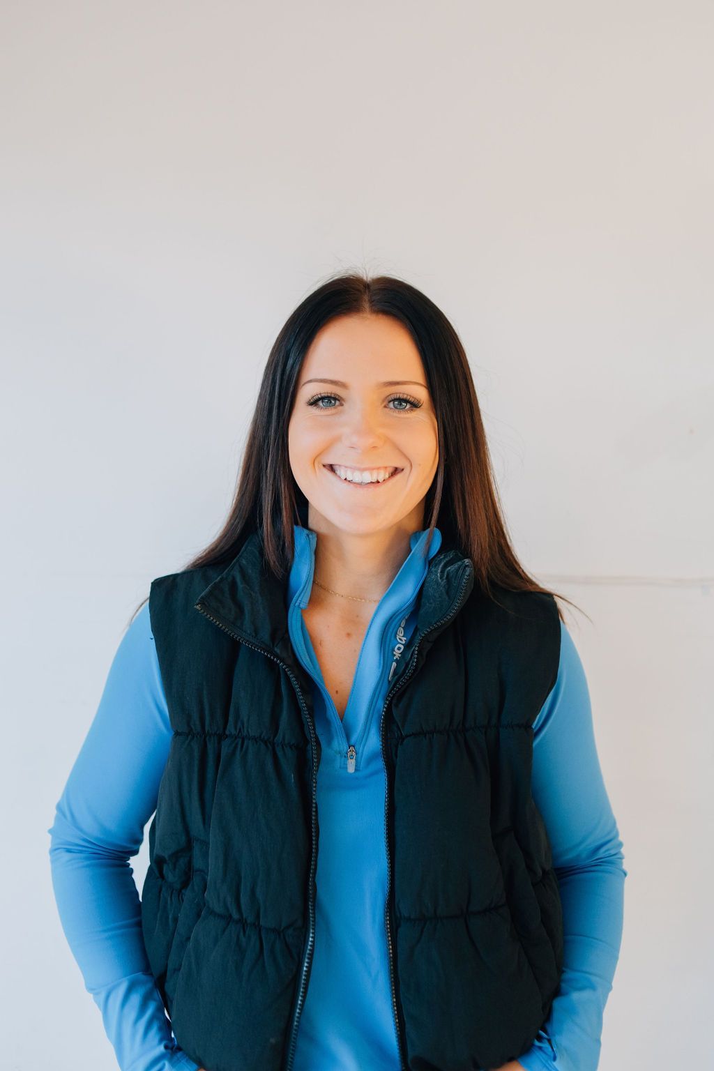 A woman wearing a black vest and a blue shirt is smiling.