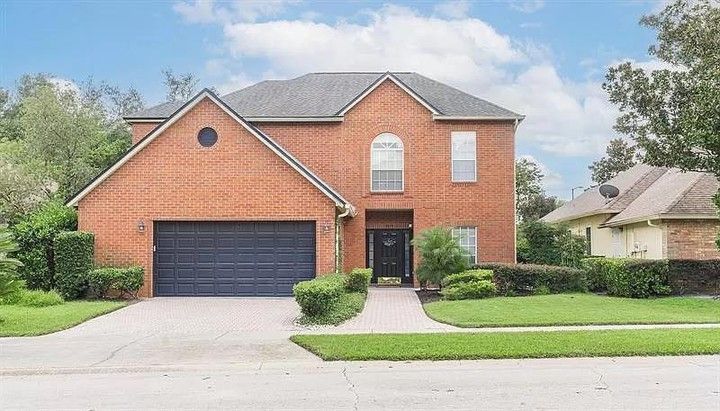 Two-story brick house with a dark garage door, front lawn, and driveway on a suburban street