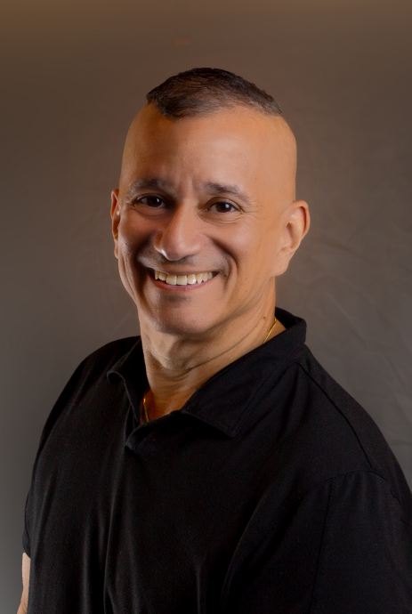 Smiling person in a black shirt against a plain brown background