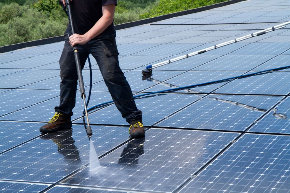 Person Power Washing Solar Panels on a Roof, Blue and Black — Ericson Constructions in Mareeba, QLD