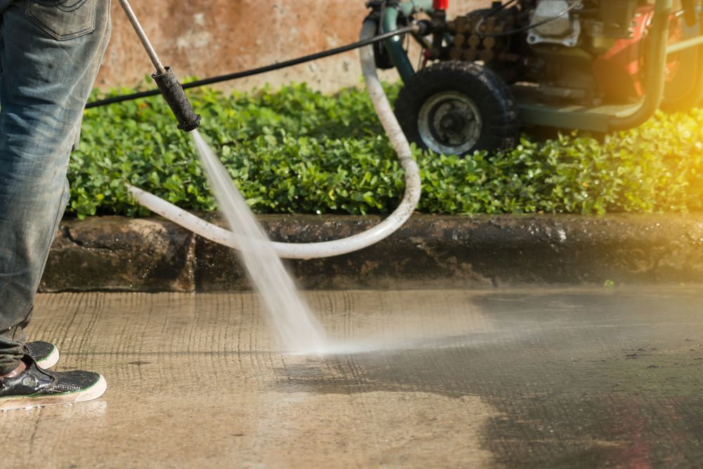 Person Power Washing a Concrete Surface With Pressure Washer Near Greenery — Ericson Constructions in Mareeba, QLD