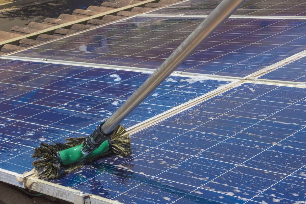 Cleaning Solar Panels With a Long-handled Brush on a Rooftop — Ericson Constructions in Mareeba, QLD
