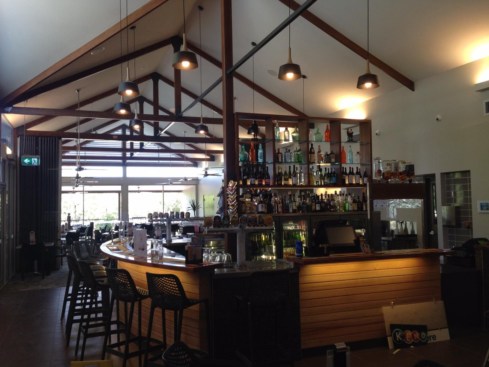 Bar with wood paneling, dark stools, drinks, and open view.