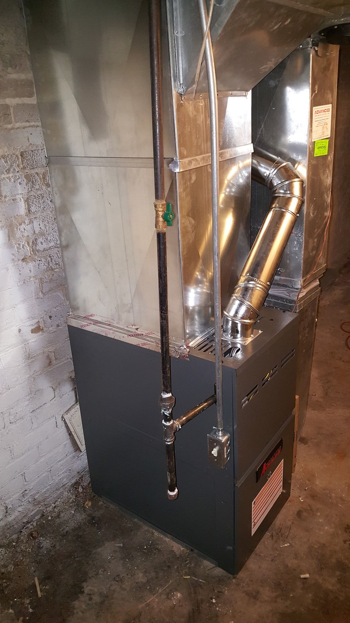 a furnace is sitting in a basement next to a brick wall .