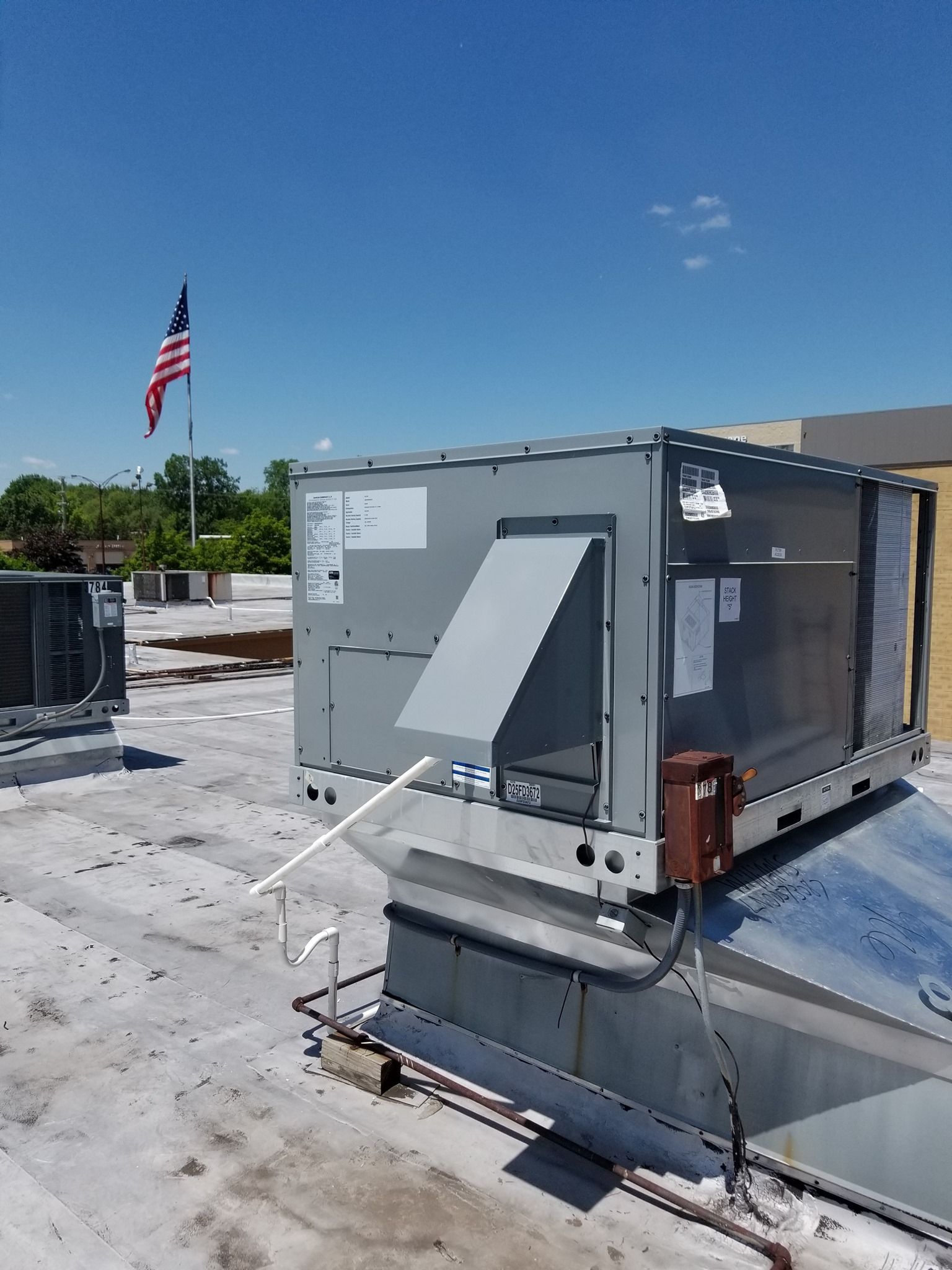 a large air conditioner is sitting on top of a roof with an american flag in the background .