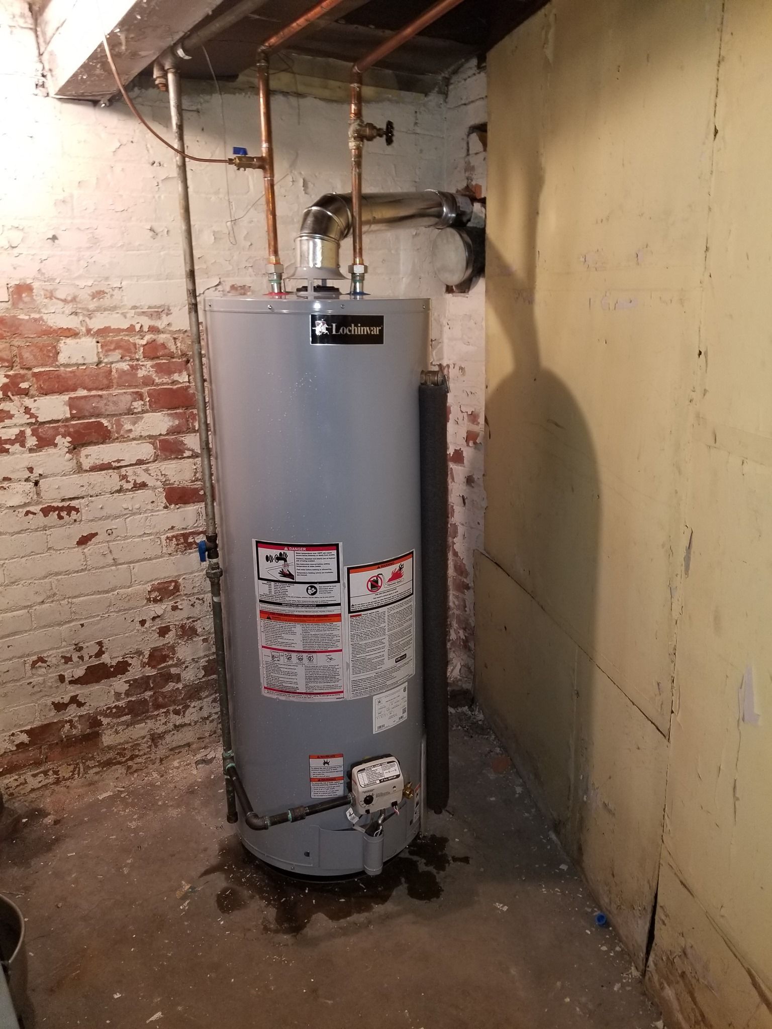 a water heater is sitting in a basement next to a brick wall .