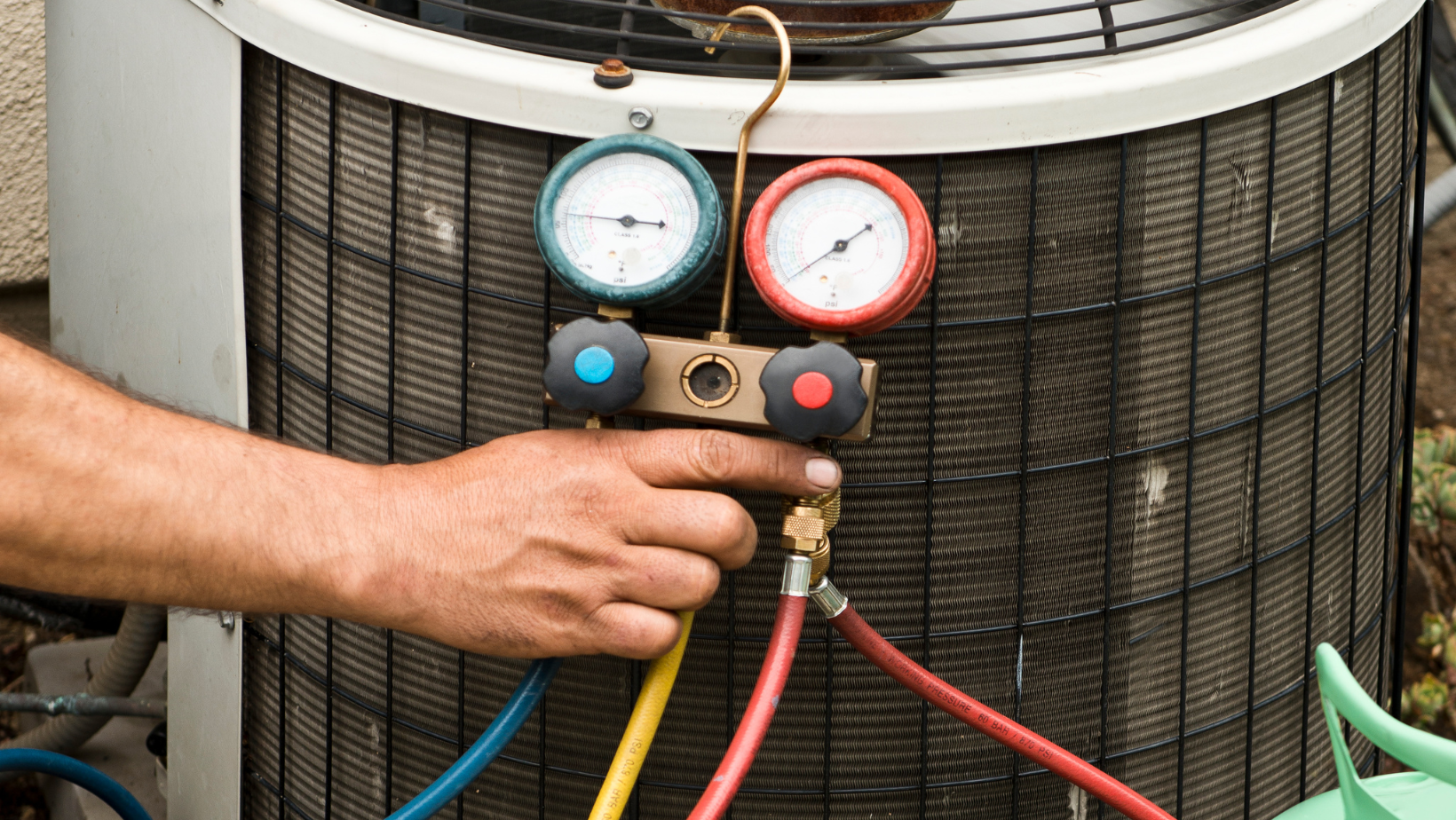 a man is working on an air conditioner with gauges attached to it .