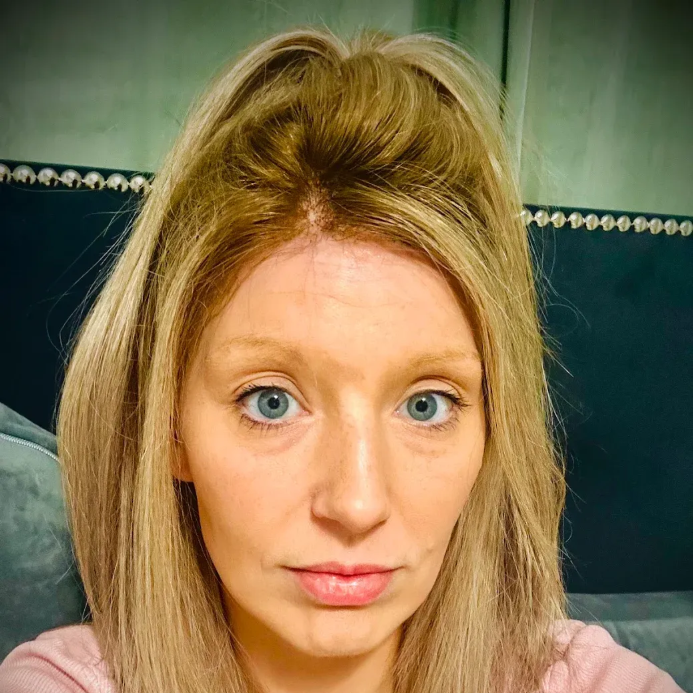 Woman with blonde hair pulled back, light eyes, and neutral expression. Indoor setting.