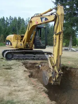 A yellow cat excavator is digging a hole in the ground
