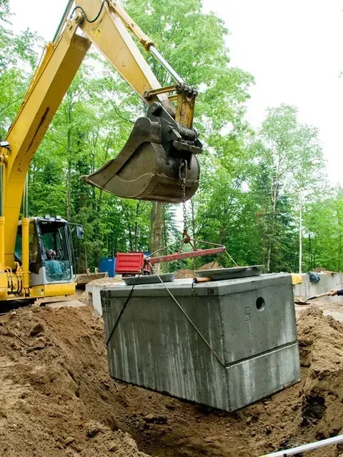 A yellow excavator is lifting a large concrete block out of the ground.