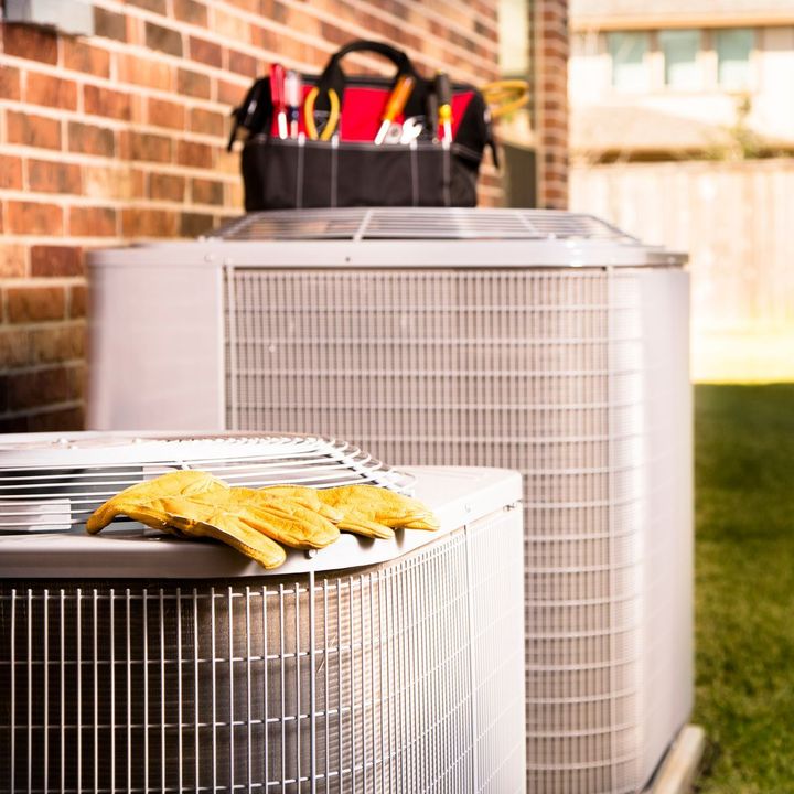 Two air conditioners are sitting next to each other in front of a brick building.