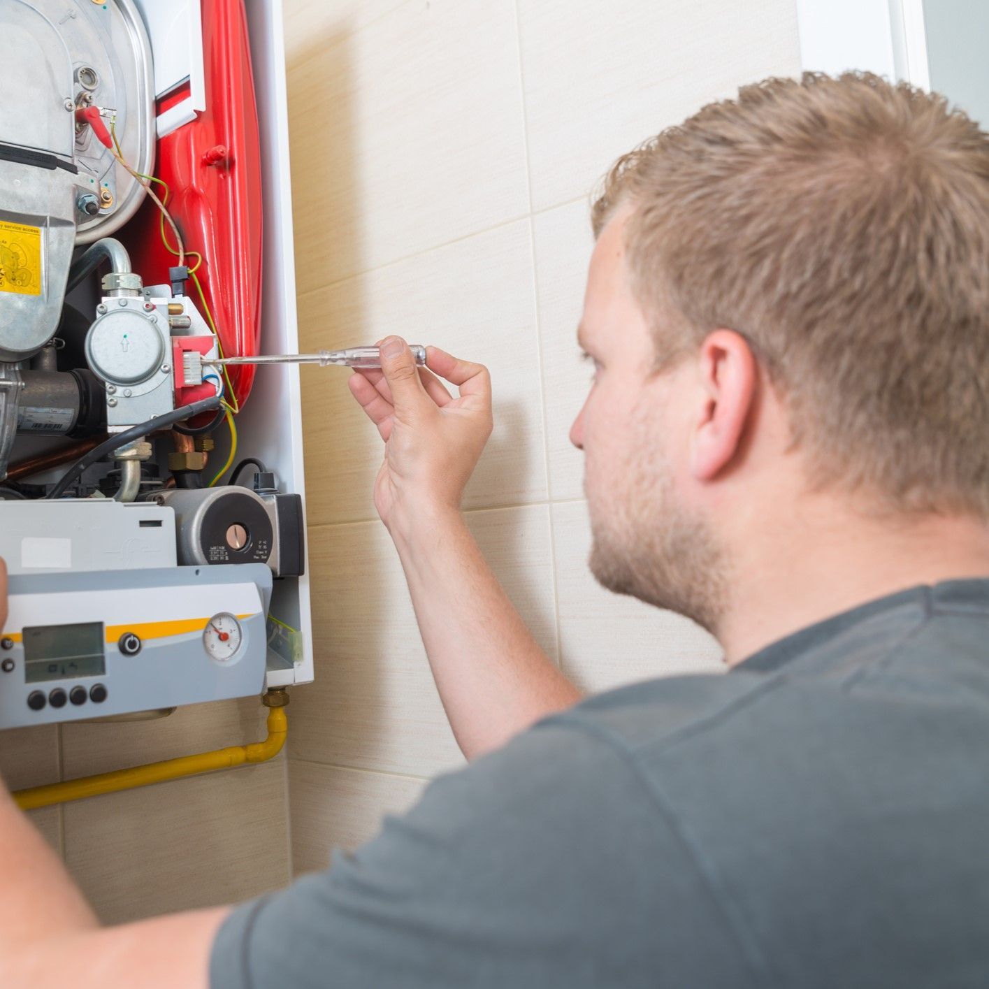 A man is fixing a boiler with a screwdriver A man is fixing a boiler with a screwdriver