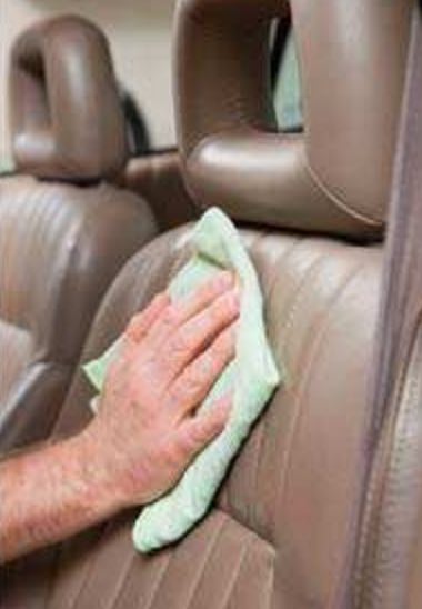 A person is cleaning a car seat with a cloth.