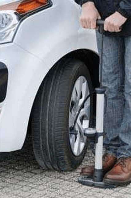A man is pumping the tire of a white car with a tire pump.