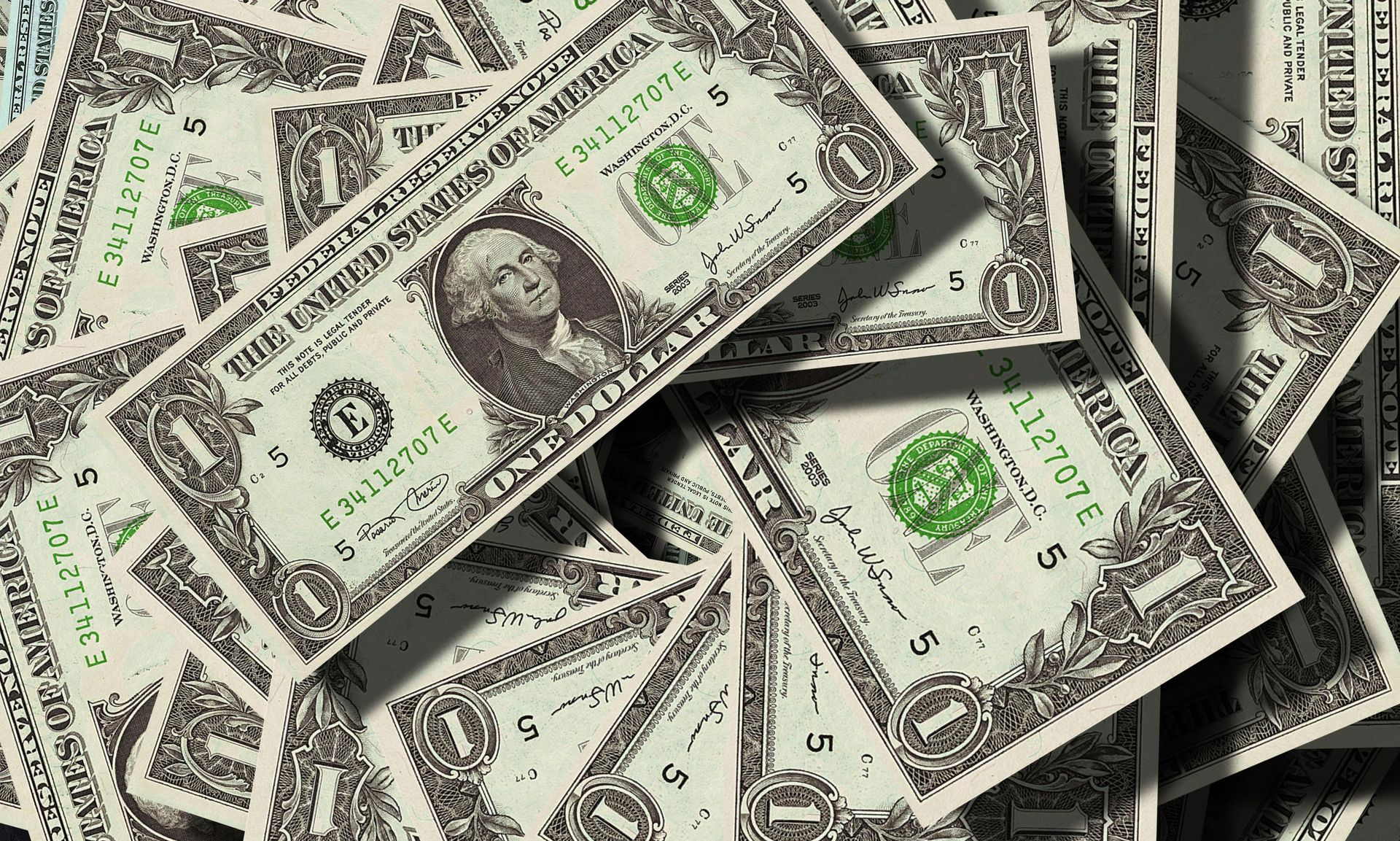 Scattered US one-dollar bills in a close-up pile, showing George Washington portraits and green seals